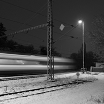 Noční vlak projíždí zasněženým nádražím.