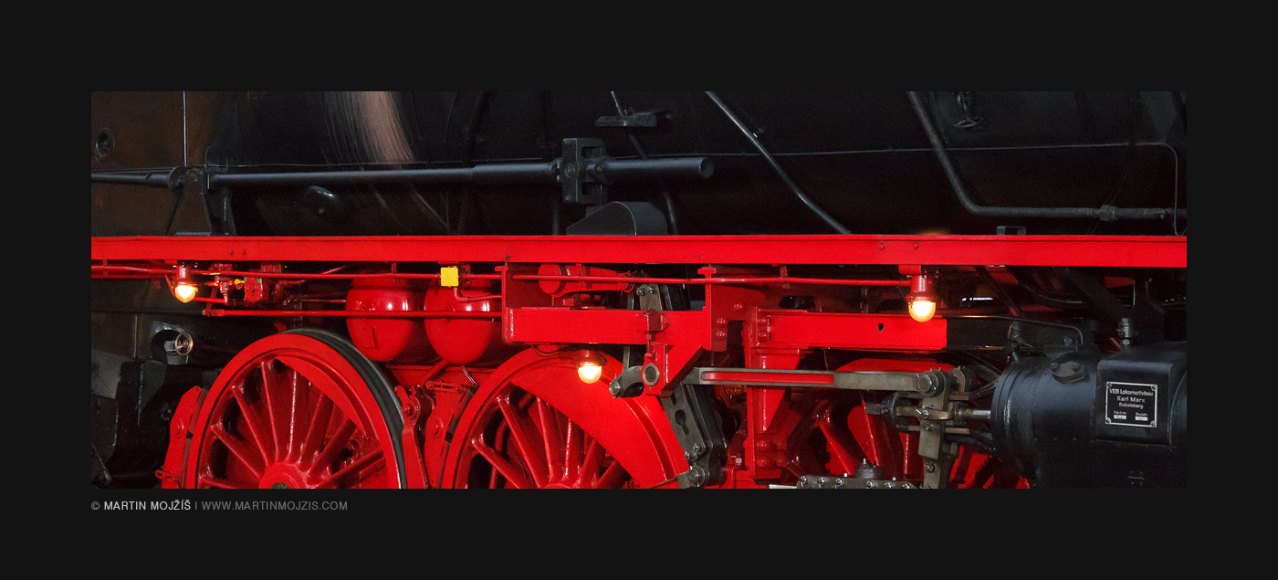 Pohled zblízka na precizně zrekonstruovaný podvozek parní lokomotivy s funkčními, svítícími lampičkami.