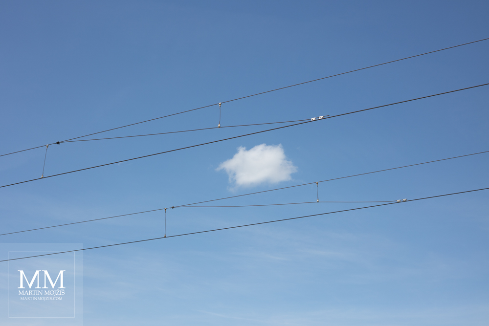 Fotografie železničního trolejového vedení a modrého nebe s bílým mráčkem, zhotovená objektivem Canon EF 50 mm 1:1.8 STM při testu / recenzi.