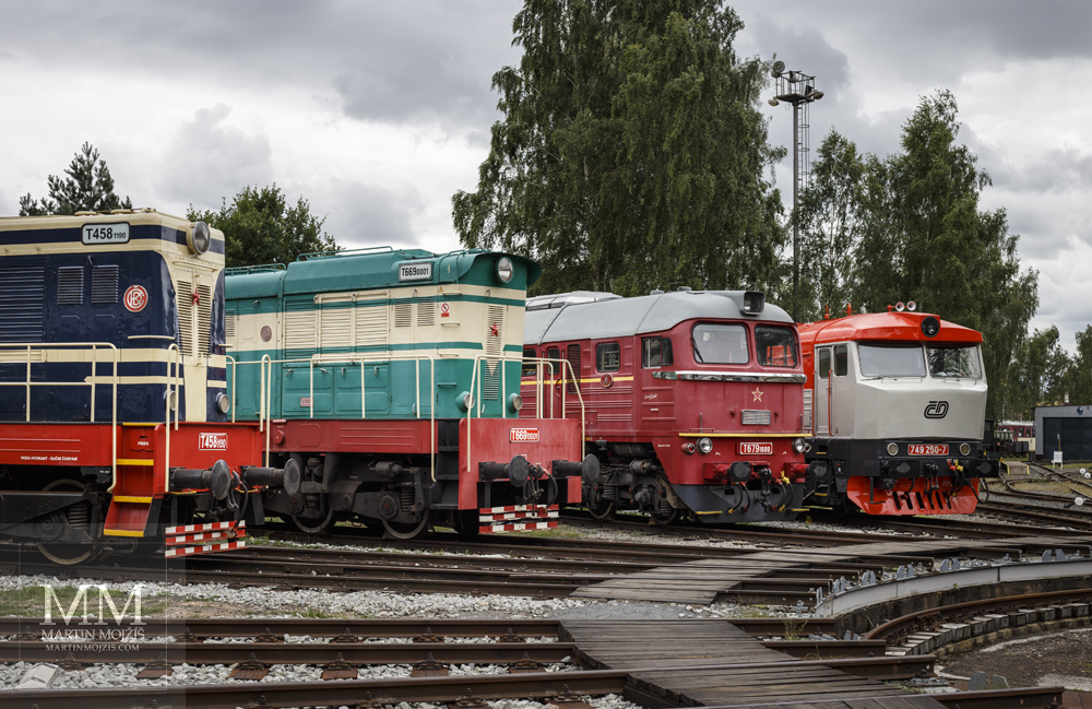 Fotografie diesel-elektrických lokomotiv Velký Hektor, Čmelák, Sergej (Serjoža) a Bardotka (Mračoun, Zamračená) u točny. Vytvořena objektivem Canon EF 50 mm 1:1.8 STM.