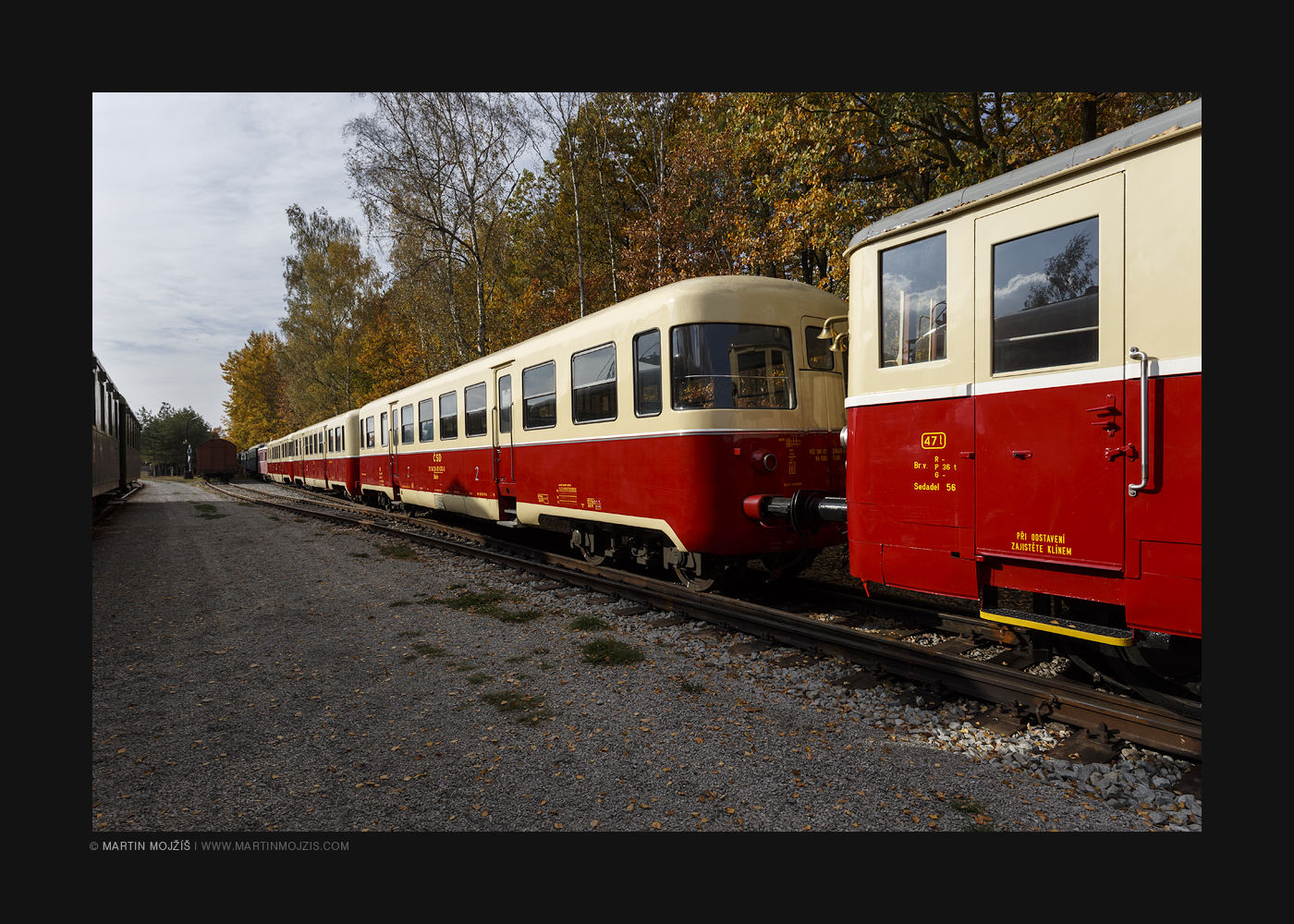 Krémově žluté a červené historické železniční vagony v podzimním slunci.
