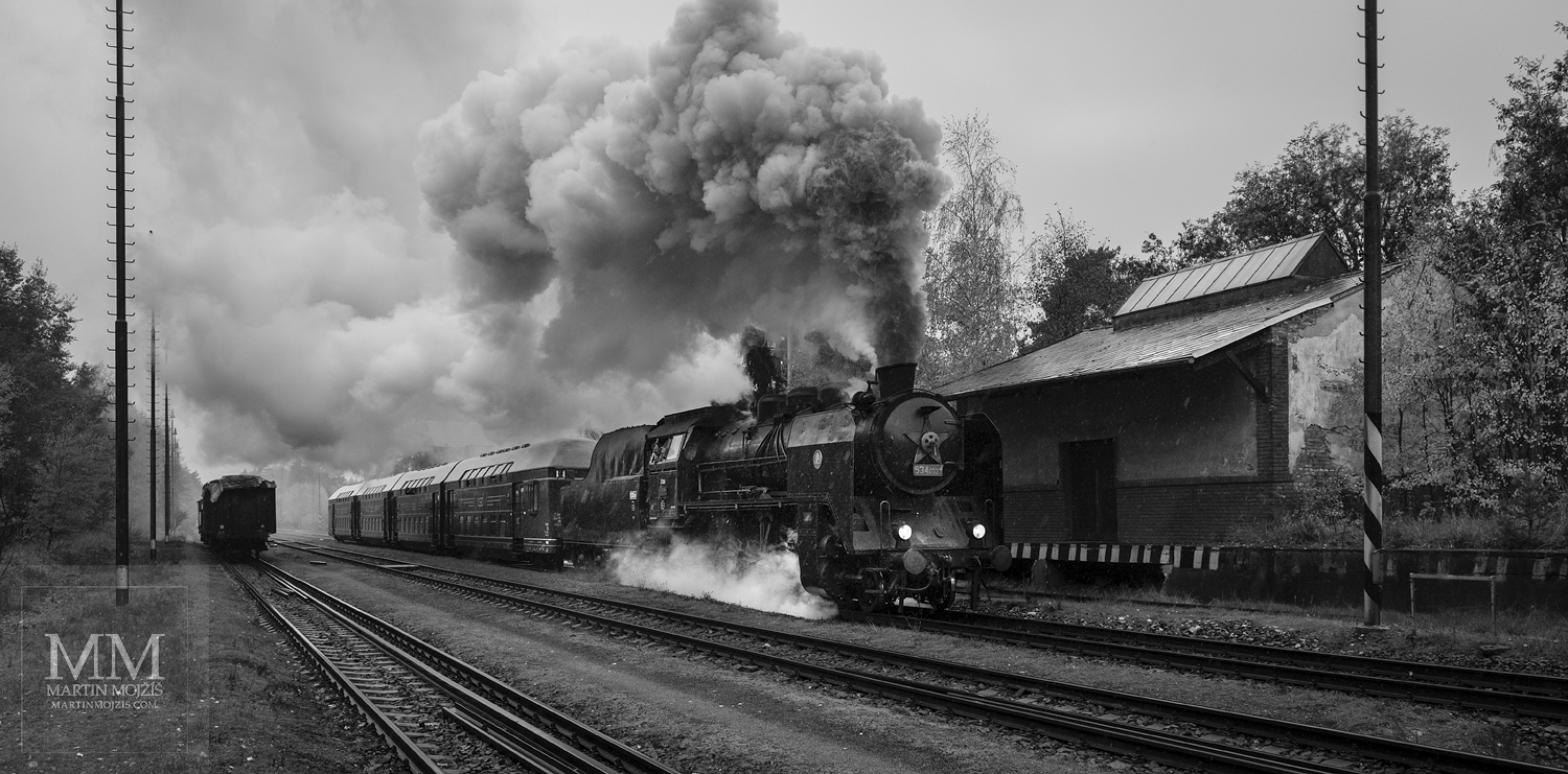Velkoformátová černobílá umělecká fotografie parní lokomotivy v čele osobního vlaku. Martin Mojžíš.