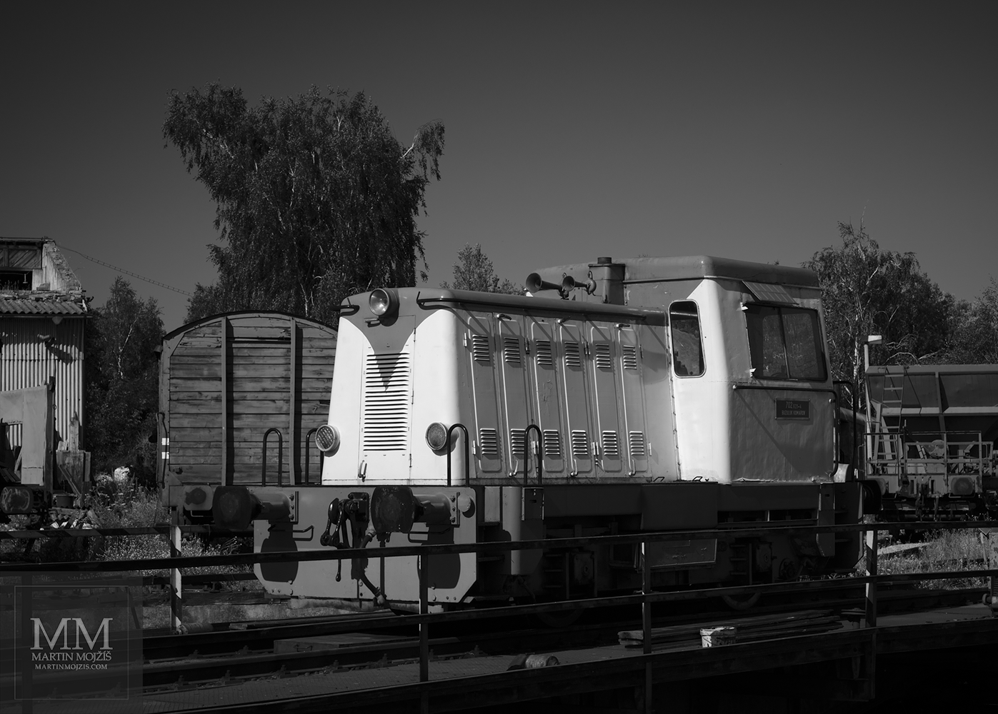 Malá dieselová lokomotiva 702 621-4 Buzuluk Komárov stojící na točně. Umělecká černobílá fotografie s názvem ODPOČINEK V POLOVINĚ LÉTA II. Fotograf Martin Mojžíš.