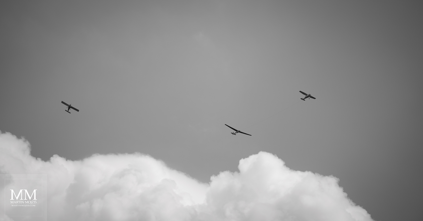 Tři letící letadla, bílý mrak. Umělecká černobílá fotografie s názvem NA POČÁTKU LÉTA II. Fotograf Martin Mojžíš.