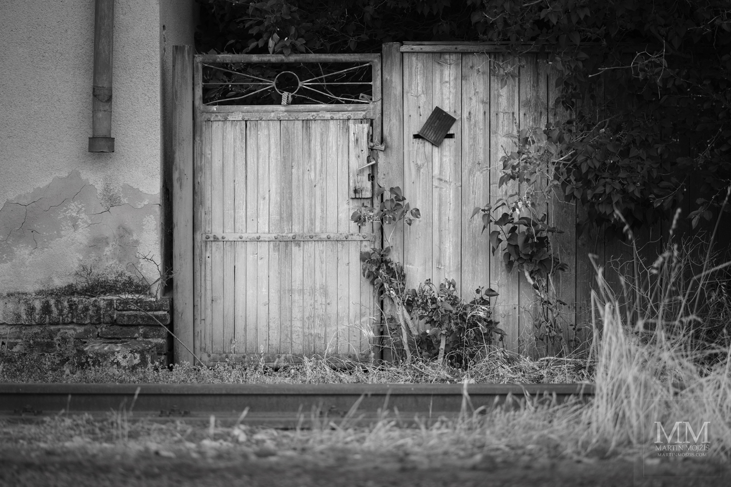 Branka do zahrady u kolejí. Umělecká černobílá fotografie s názvem PŘED BRANKOU – KOLEJE. Fotograf Martin Mojžíš.
