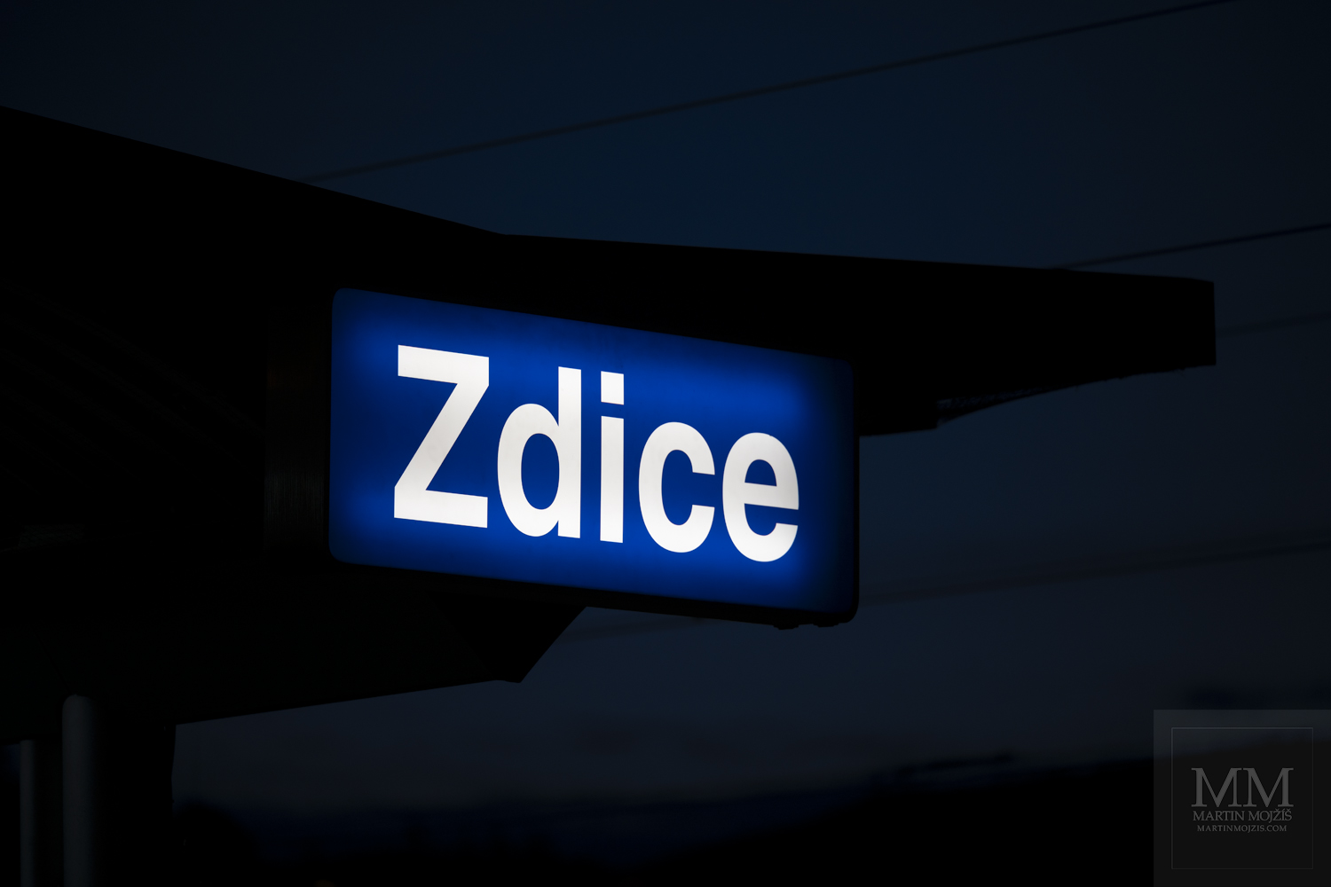 A illuminated name of the Zdice railway station at dusk. Fine art photograph EVENINGS IN ZDICE, photographed by Martin Mojzis.