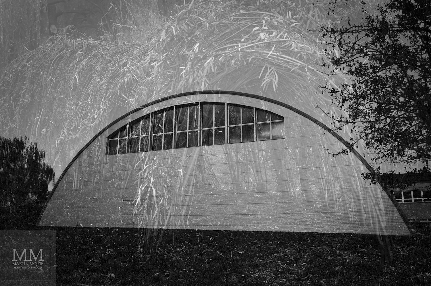 Fotografie sportovní haly prolnutá se stavbou z proutí. Umělecká černobílá fotografie Martina Mojžíše s názvem V ČASE.