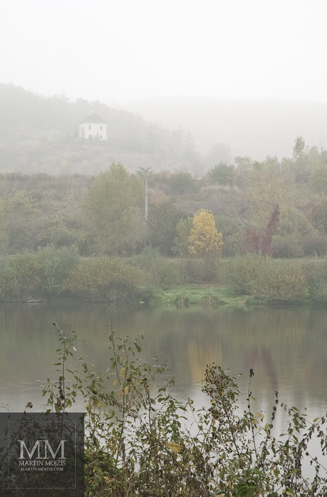 Podzim u řeky, barevné listy, v pozadí malý domek v mlze. Umělecká fotografie Martina Mojžíše s názvem DNES MOŽNÁ PŘIJDE ZIMA.