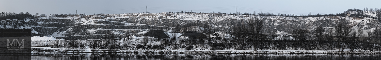 Velkoformátová, pět metrů široká fotografie velkého, zasněženého lomu u řeky v zimě. Umělecká velkoformátová fotografie Krajina lomem změněná. Fotograf Martin Mojžíš.
