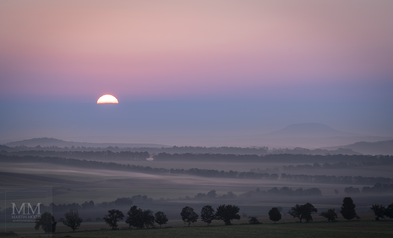 Vycházející Slunce nad krajinou, místy lehké mlhy. Umělecká velkoformátová fotografie Tichá jitra. Fotograf Martin Mojžíš.