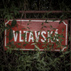 Photograph of the Vltavská street name, partly hidden behind the branches of the bushes.