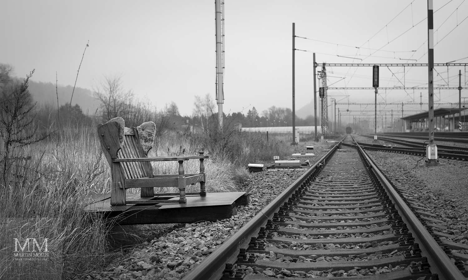 Pohovka u kolejí v železniční stanici. Umělecká černobílá fotografie Martina Mojžíše s názvem VÍTEJTE V MÉM DOMĚ VII.